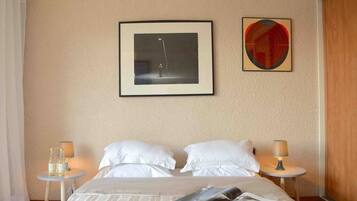 Ein Hotelzimmer mit Bett, zwei Kissen, einem gerahmten Bild, einem Tisch mit Lampe und Wandkunst in Kreisform.