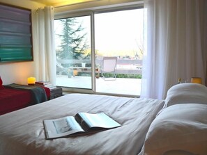 A hotel room with a large window, a bed with white bedding, a chair, and a small table with a lamp. - Casa Marta : Suites - Terrasses et vue Panoramique (Tournon-sur-Rhone)