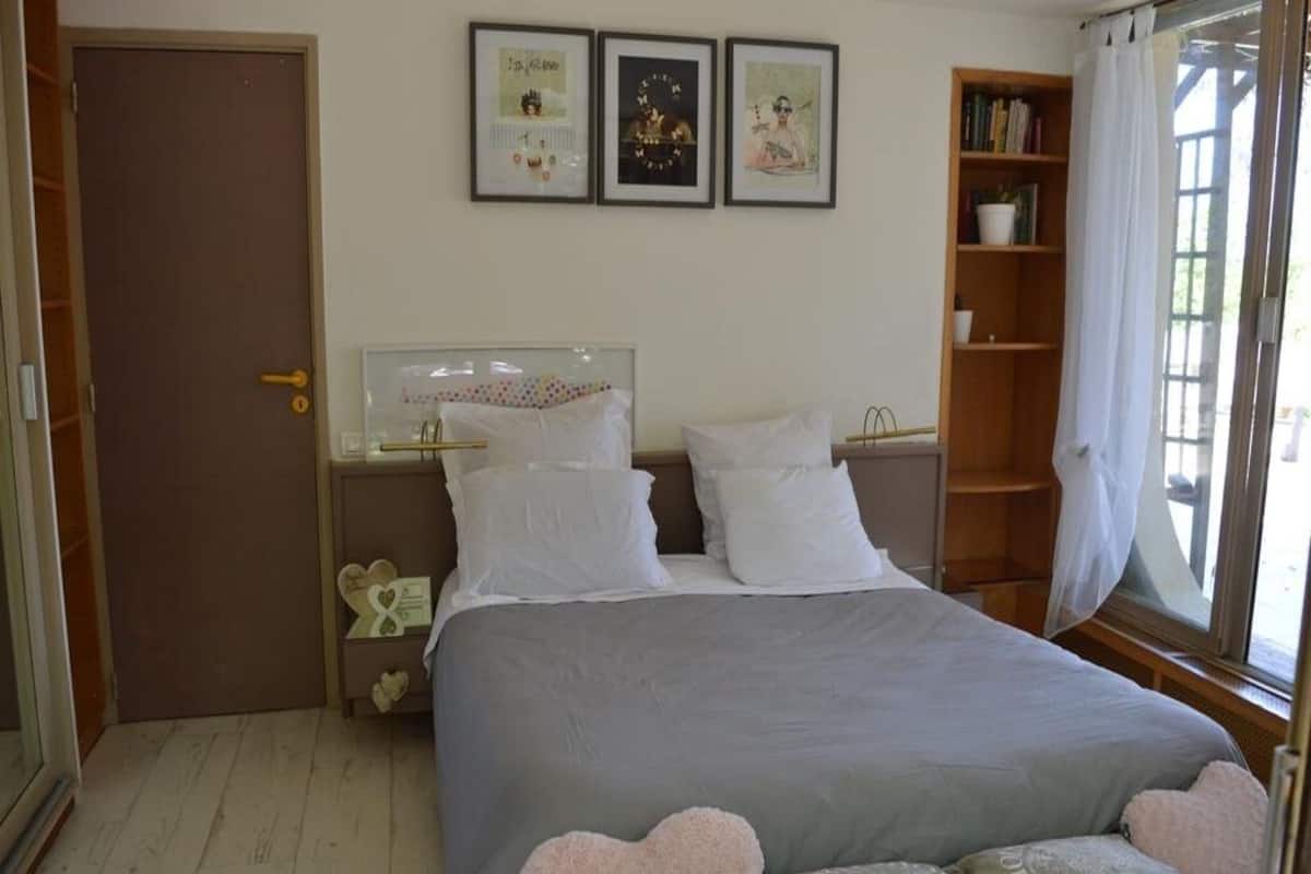 Une chambre à coucher comprenant un lit, deux tables de chevet, une commode, une fenêtre avec des rideaux et une bibliothèque.