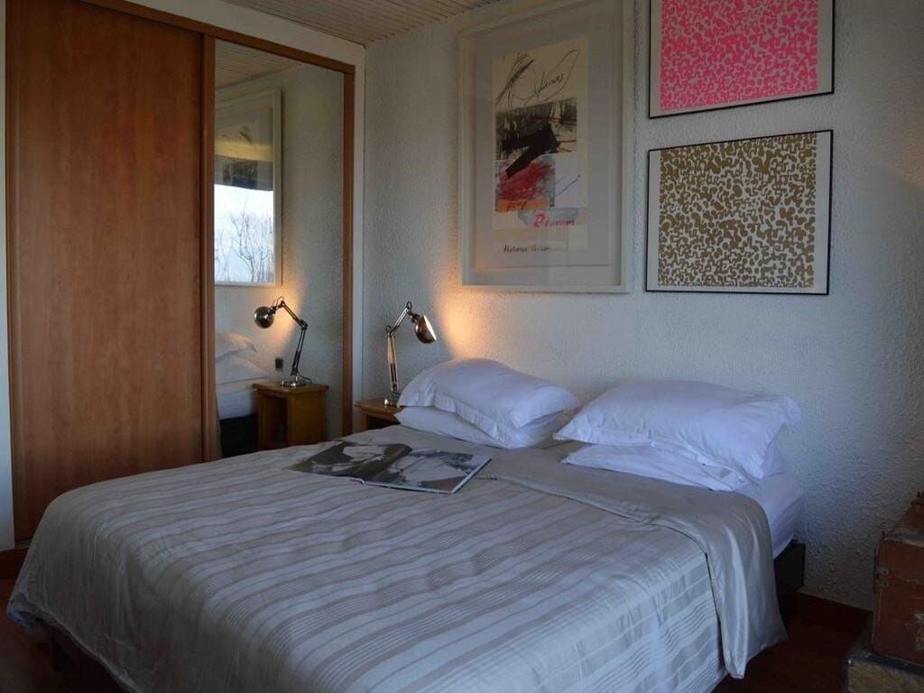 A neatly made bed with white linens and a striped blanket, a bedside lamp, and framed artwork on the wall.