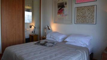 A neatly made bed with white linens and a striped blanket, a bedside lamp, and framed artwork on the wall.