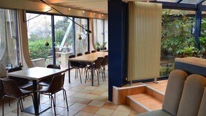 A modern dining area with a large table and chairs, a sofa, and a view of greenery through large windows. - Casa Marta : Suites - Terrasses et vue Panoramique (Tournon-sur-Rhone)