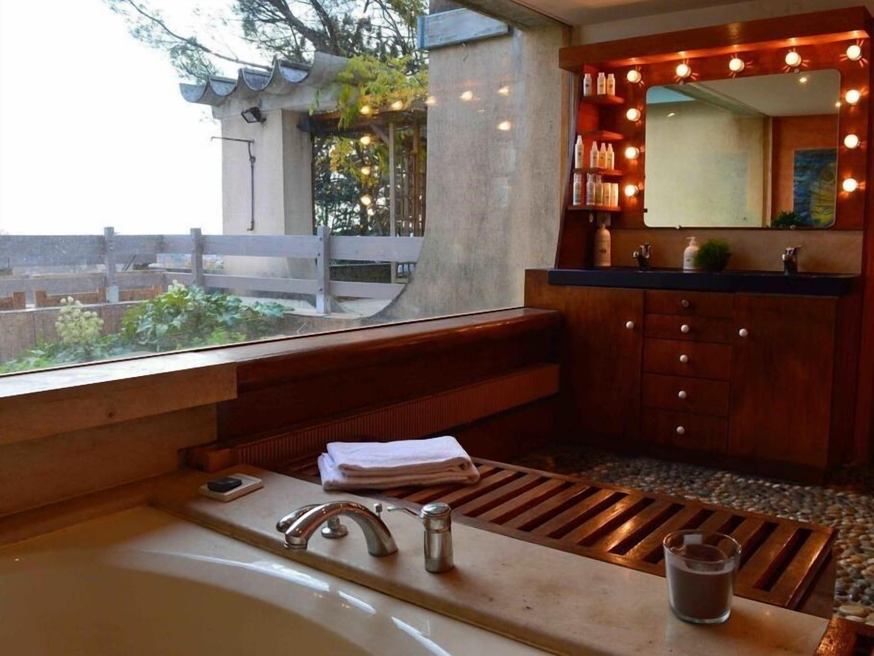 Une salle de bain dotée d’une grande fenêtre, d’un meuble-lavabo en bois, d’un évier et d’un miroir avec éclairage.