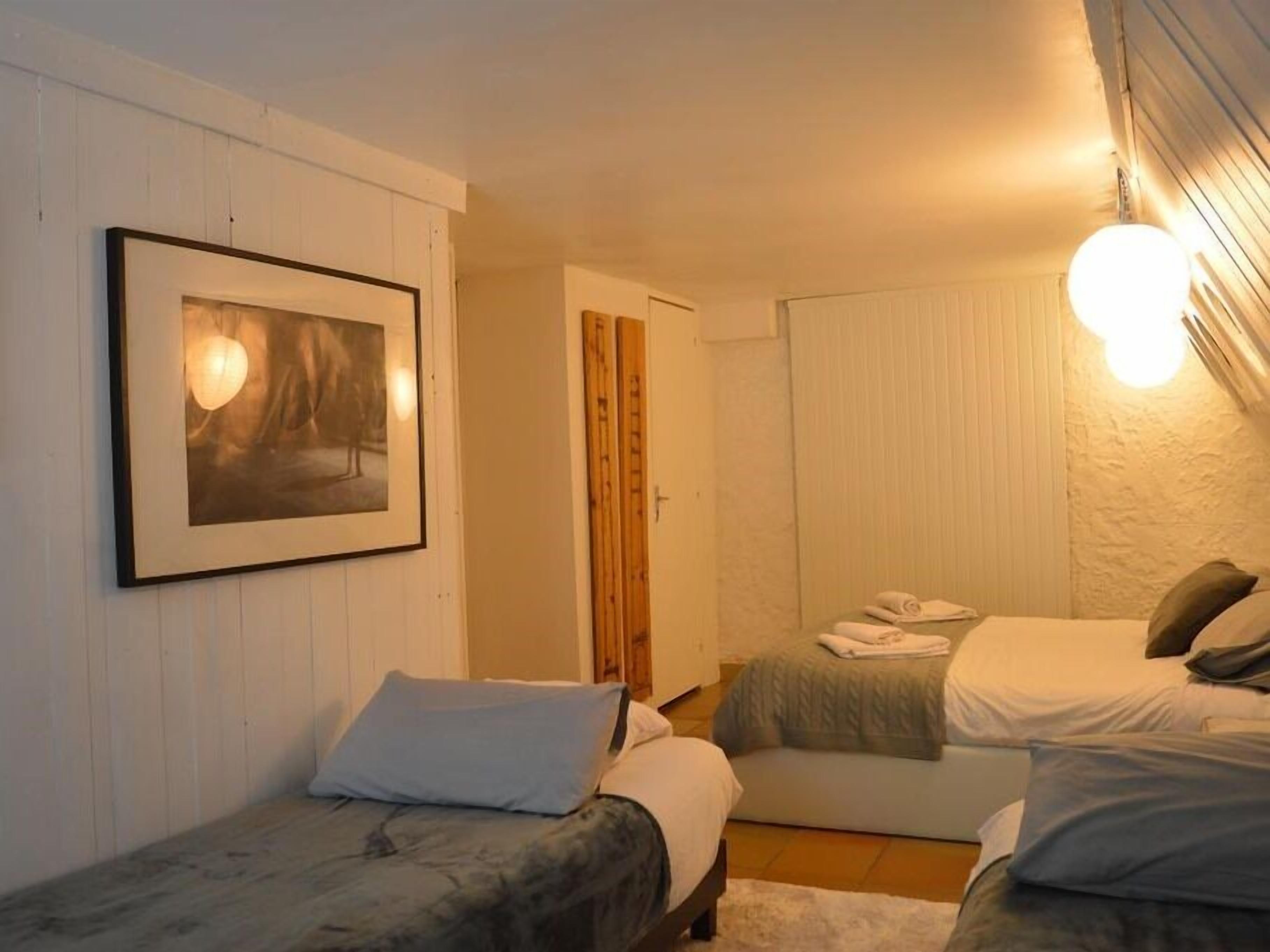 Une chambre avec deux lits, un tableau encadré au mur et une porte donnant sur une autre pièce.