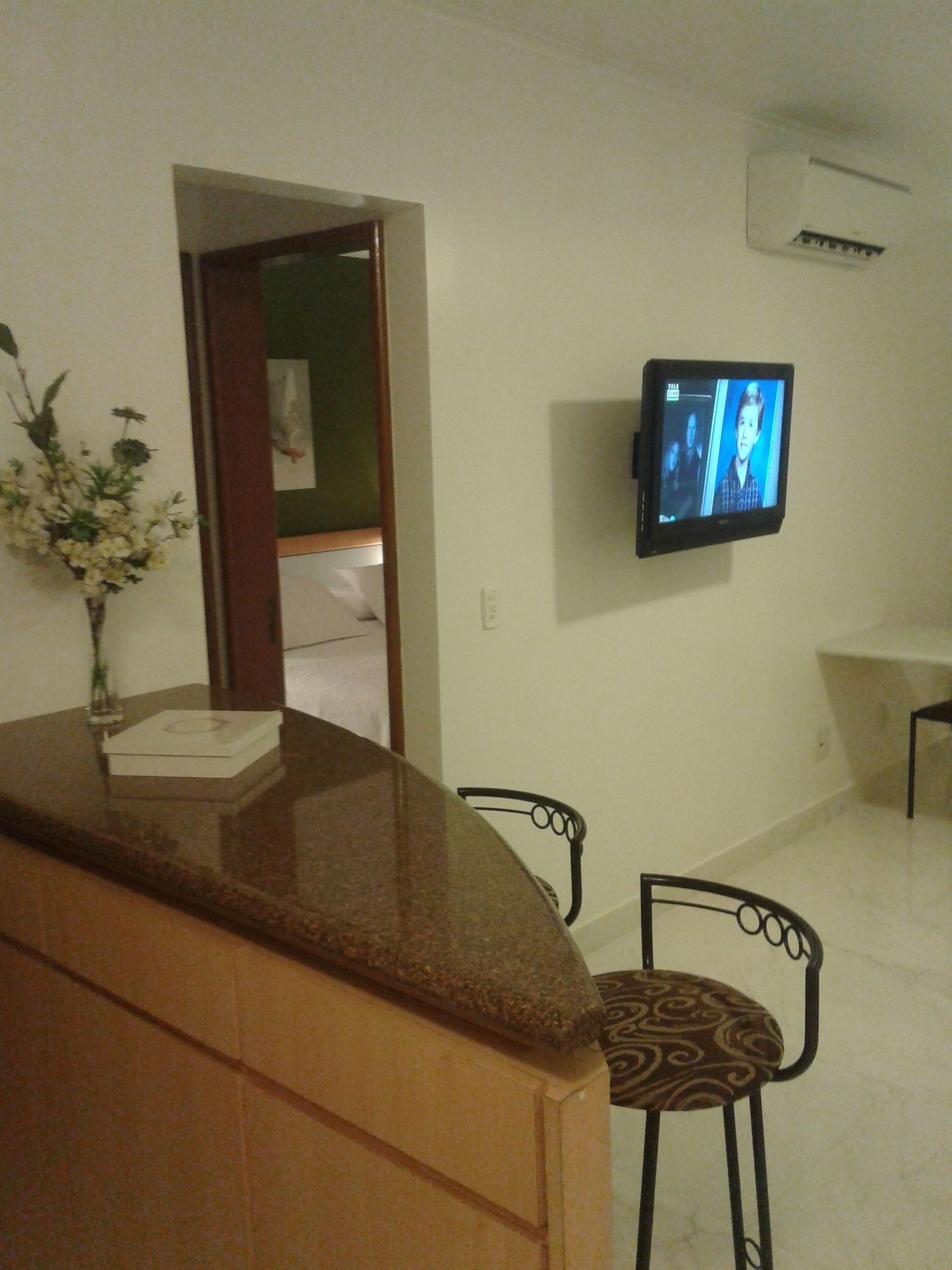 A small kitchenette with a countertop, a vase with flowers, and a television mounted on the wall.