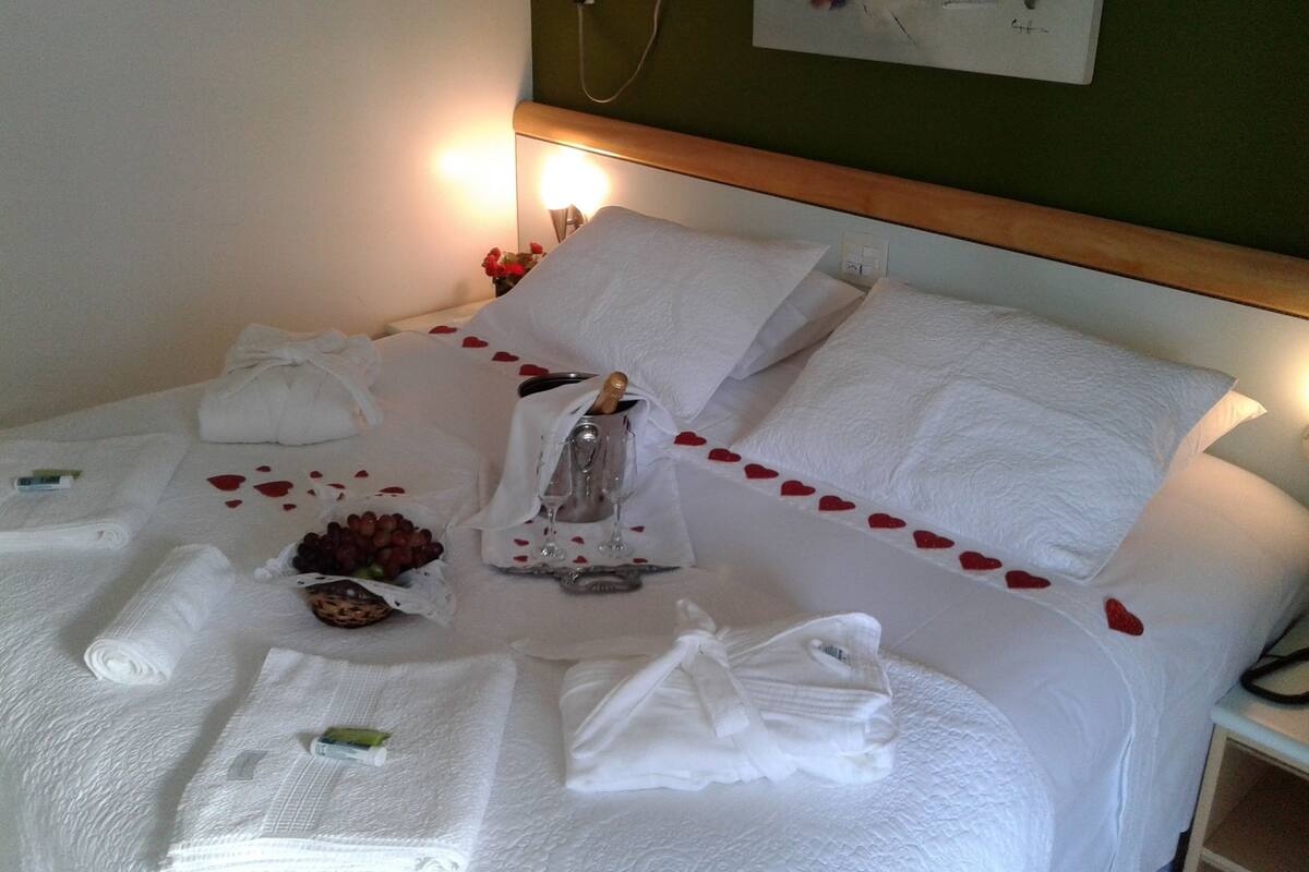 Un lit parfaitement fait, avec du linge de lit blanc, une bouteille de champagne et un petit bouquet de fleurs.