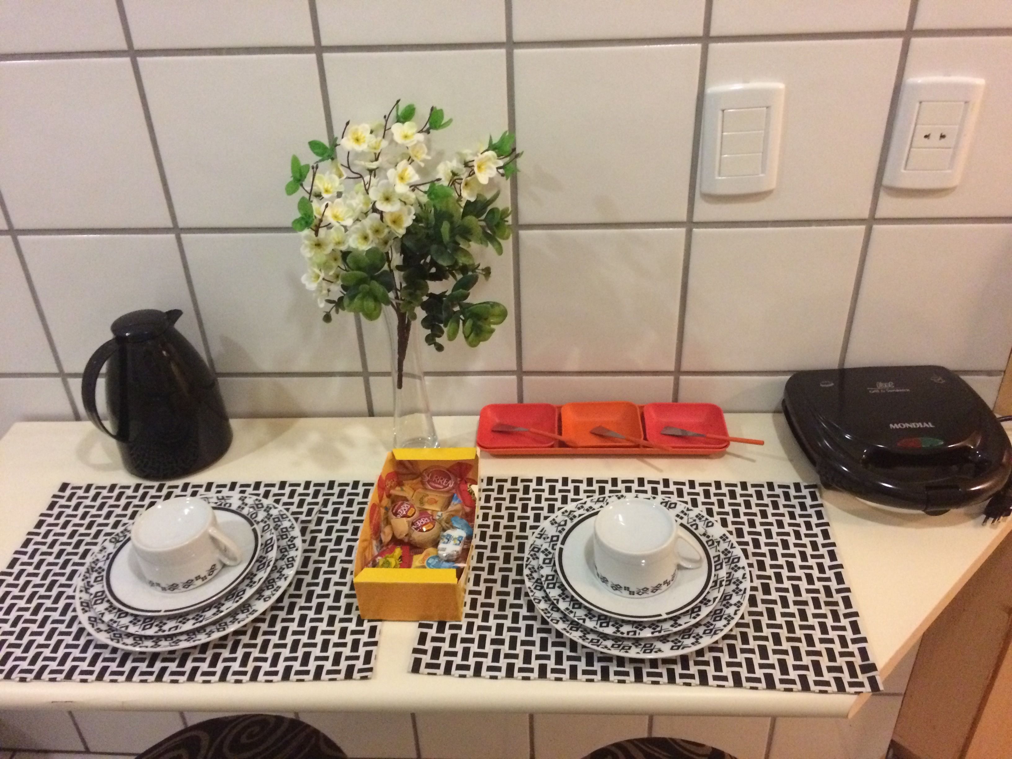 A kitchen counter with a coffee maker, a vase with flowers, a box of snacks, and a portable electric kettle.