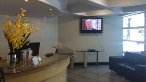 A reception area with a curved counter, a television mounted on the wall, a glass table, and a sofa. - Apart Quartier Latin Hotel (Vitoria)