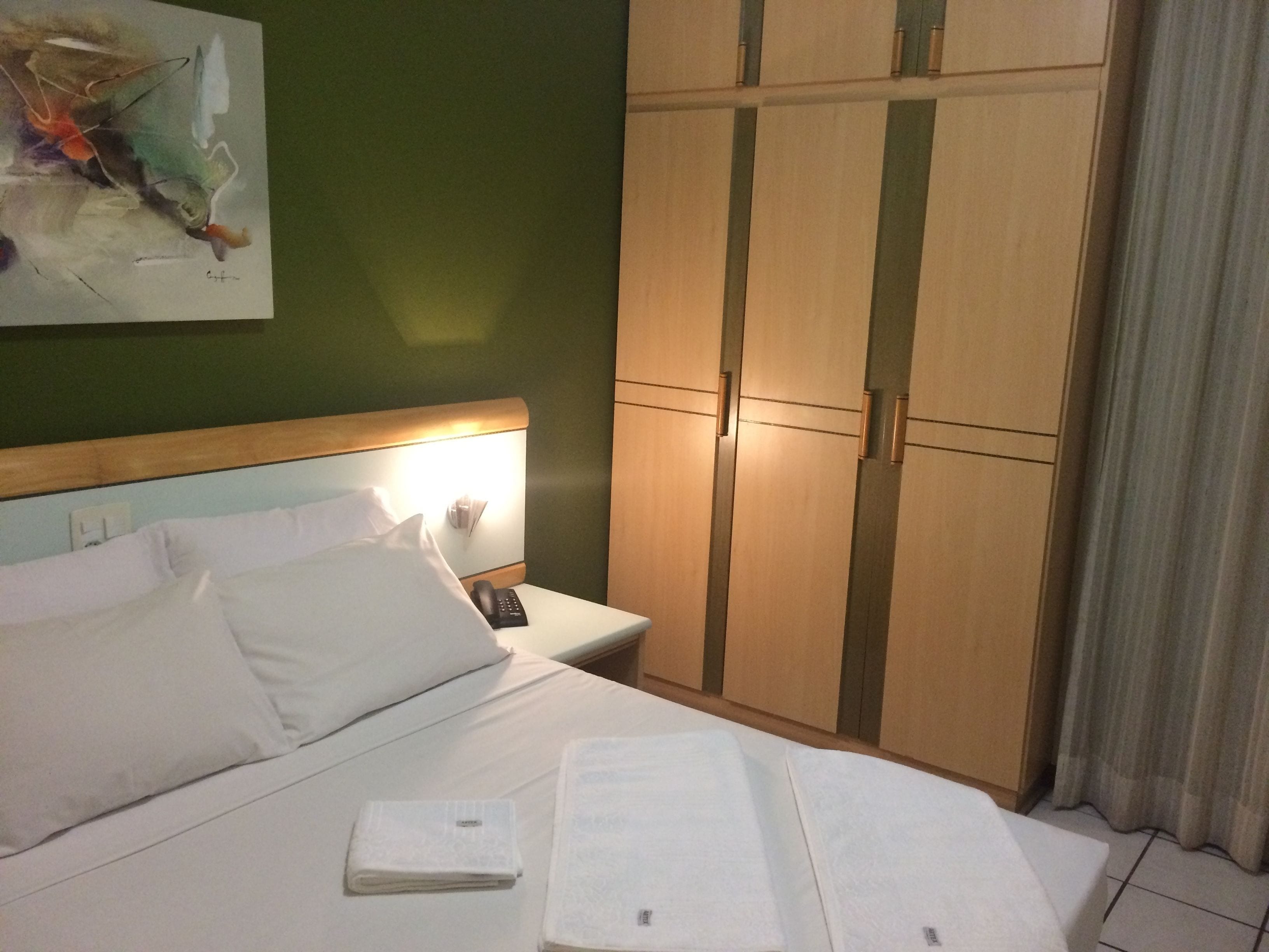 A hotel room with a bed, a nightstand, a telephone, and a wardrobe.