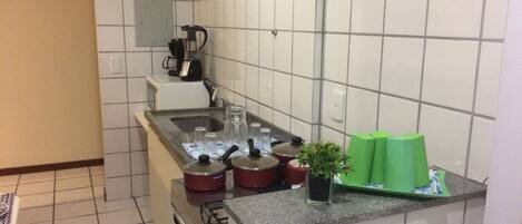A compact kitchen with a gas stove, a coffee maker, and a small potted plant.