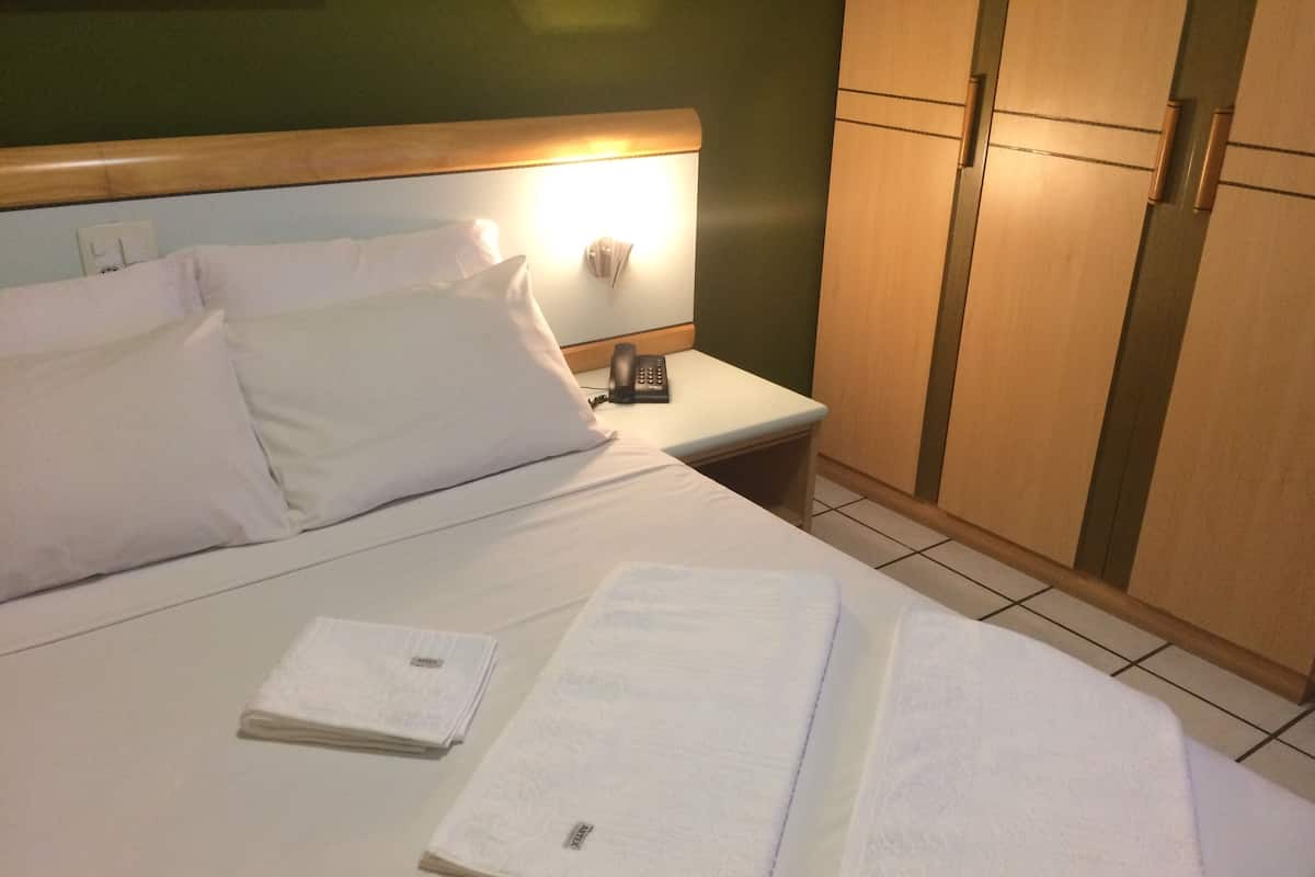Une chambre d’hôtel avec un lit, deux serviettes, une table de chevet avec un téléphone et une armoire en bois.