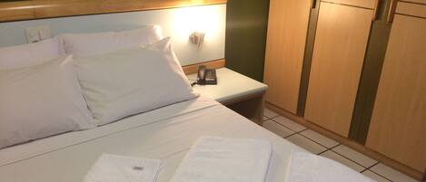 Habitación de hotel con cama, dos toallas, mesita de noche con teléfono y armario de madera.