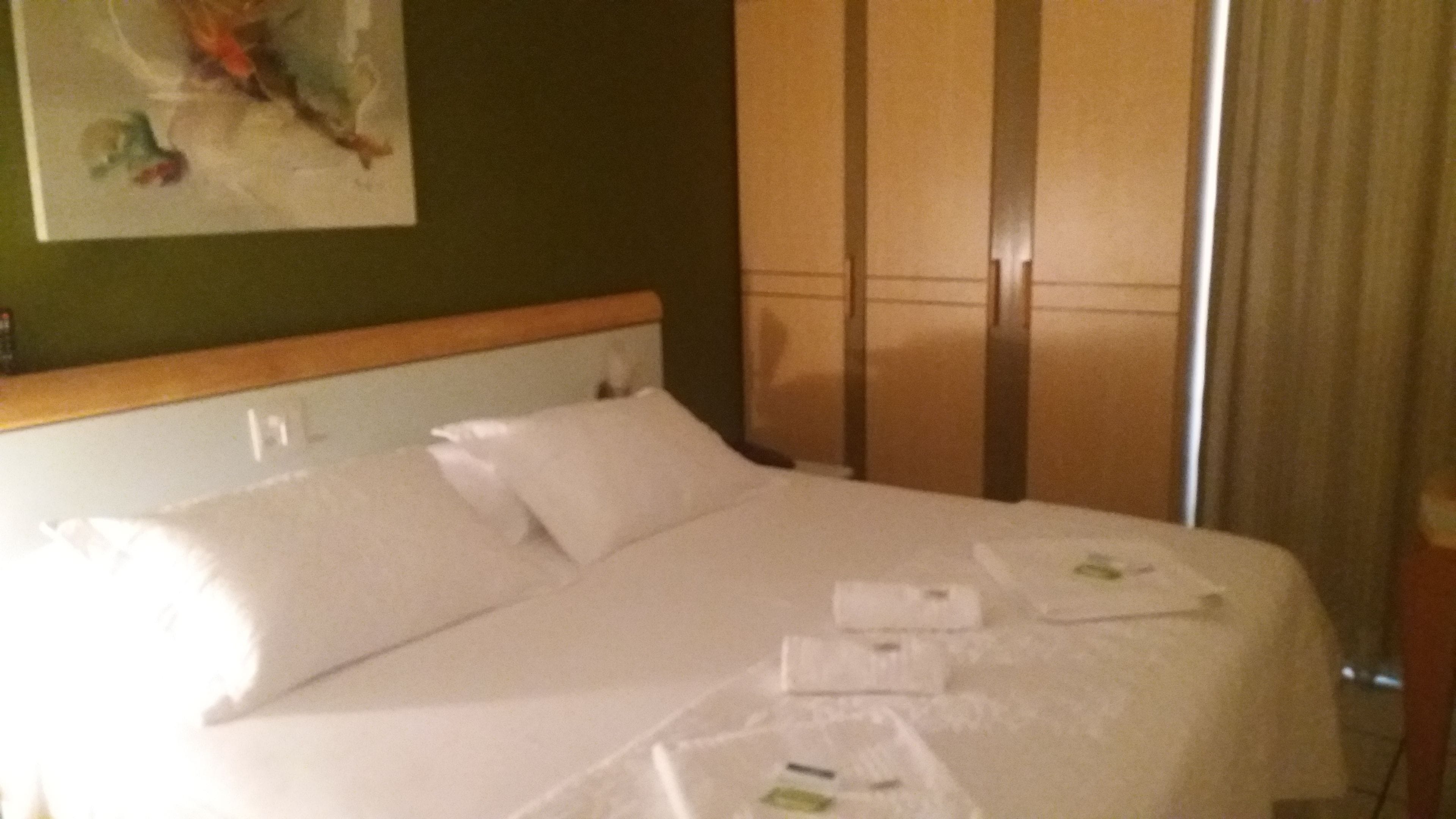 Hotelkamer met een bed, hoofdeinde, nachtkastje, schilderij aan de muur en een raam met gordijnen.