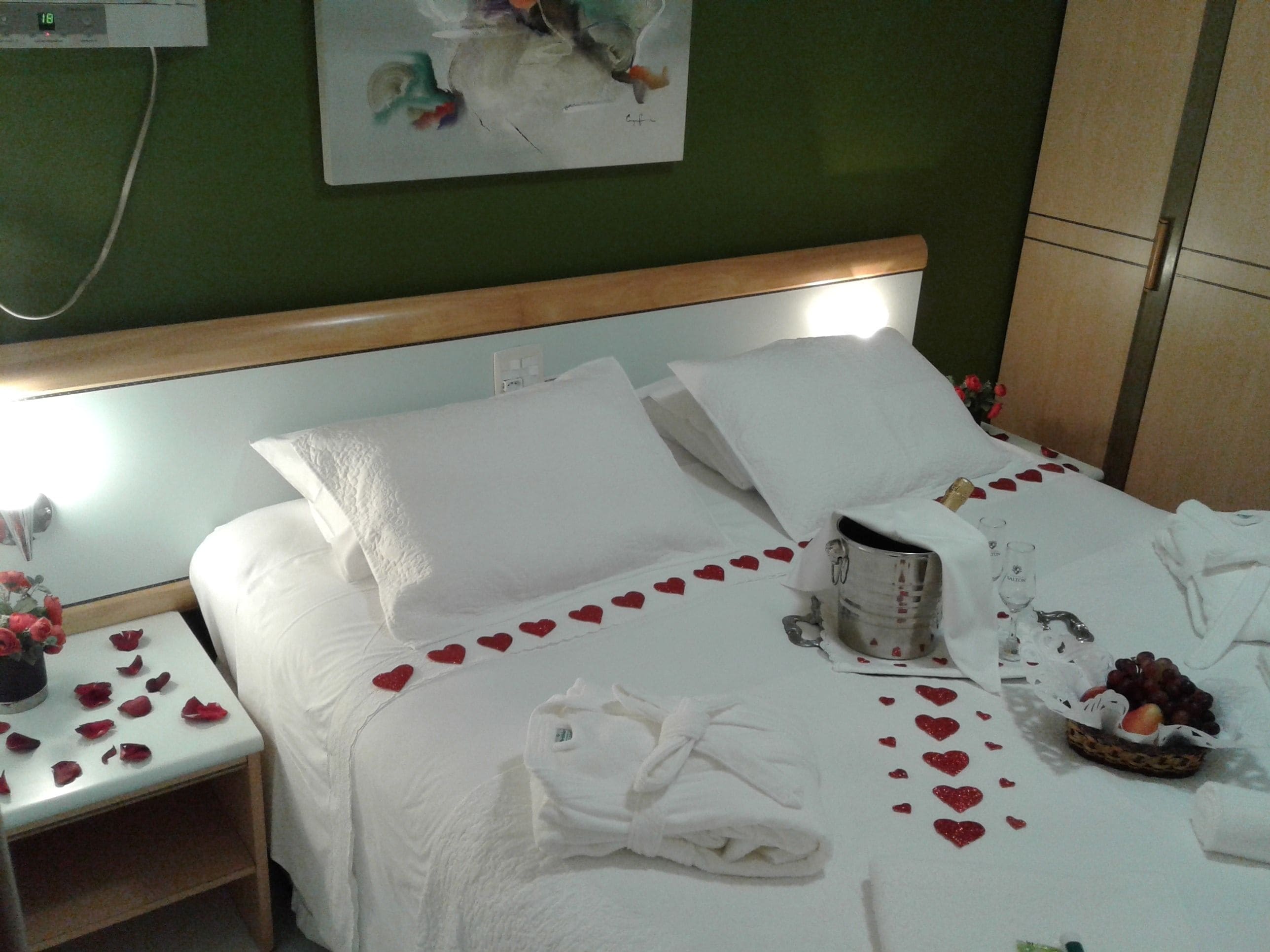 Una cama bien hecha con sábanas blancas, una mesita de noche con un jarrón de flores y un reloj de pared.