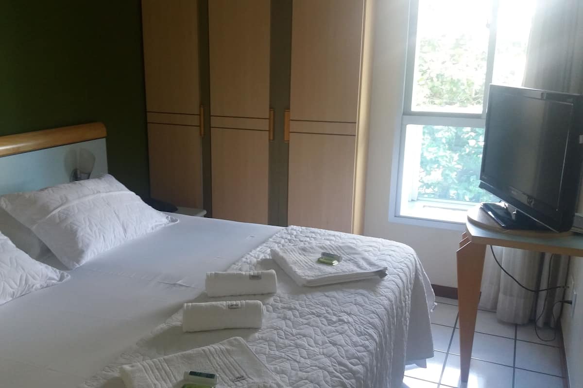 Une chambre d’hôtel avec un lit, un téléviseur posé sur un meuble et une fenêtre donnant sur un paysage verdoyant.