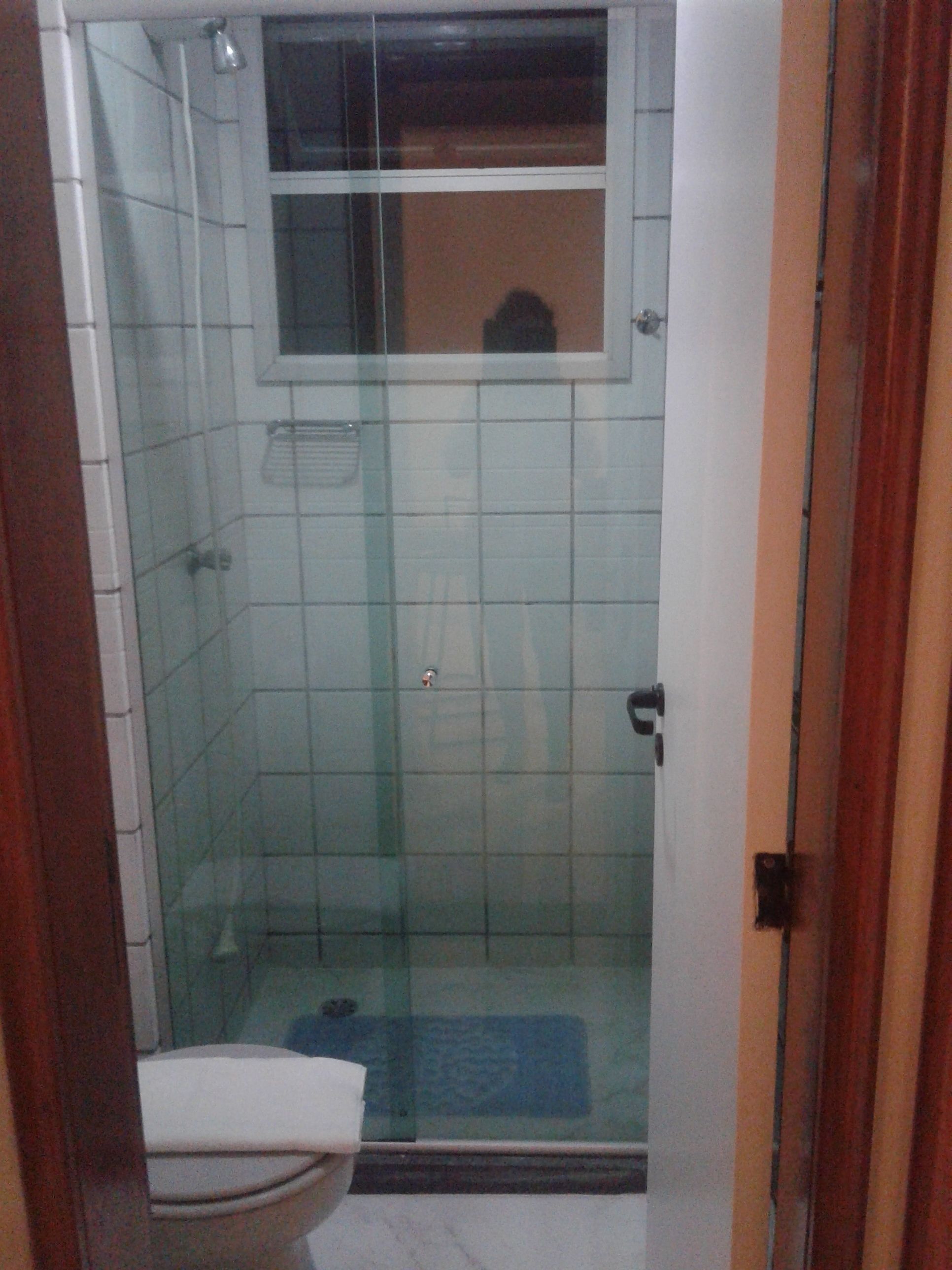 Cabina de bany amb vidre, sòl de rajoles blanques, una finestra petita i una porta.