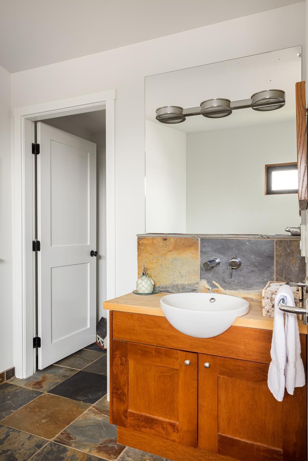 A bathroom with a white sink, wooden vanity, and a mirror with lights.