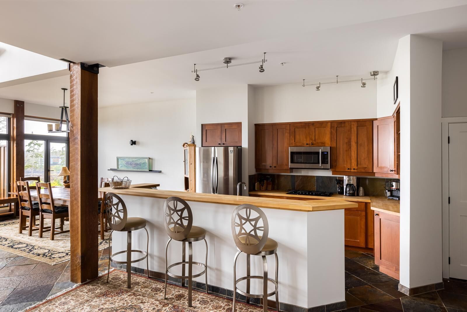 A modern kitchen with a central island, wooden bar stools, stainless steel appliances, and a large window providing natural light.