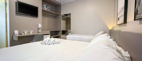 A hotel room with a large bed, a desk with a chair, a telephone, and a flat-screen TV mounted on the wall.