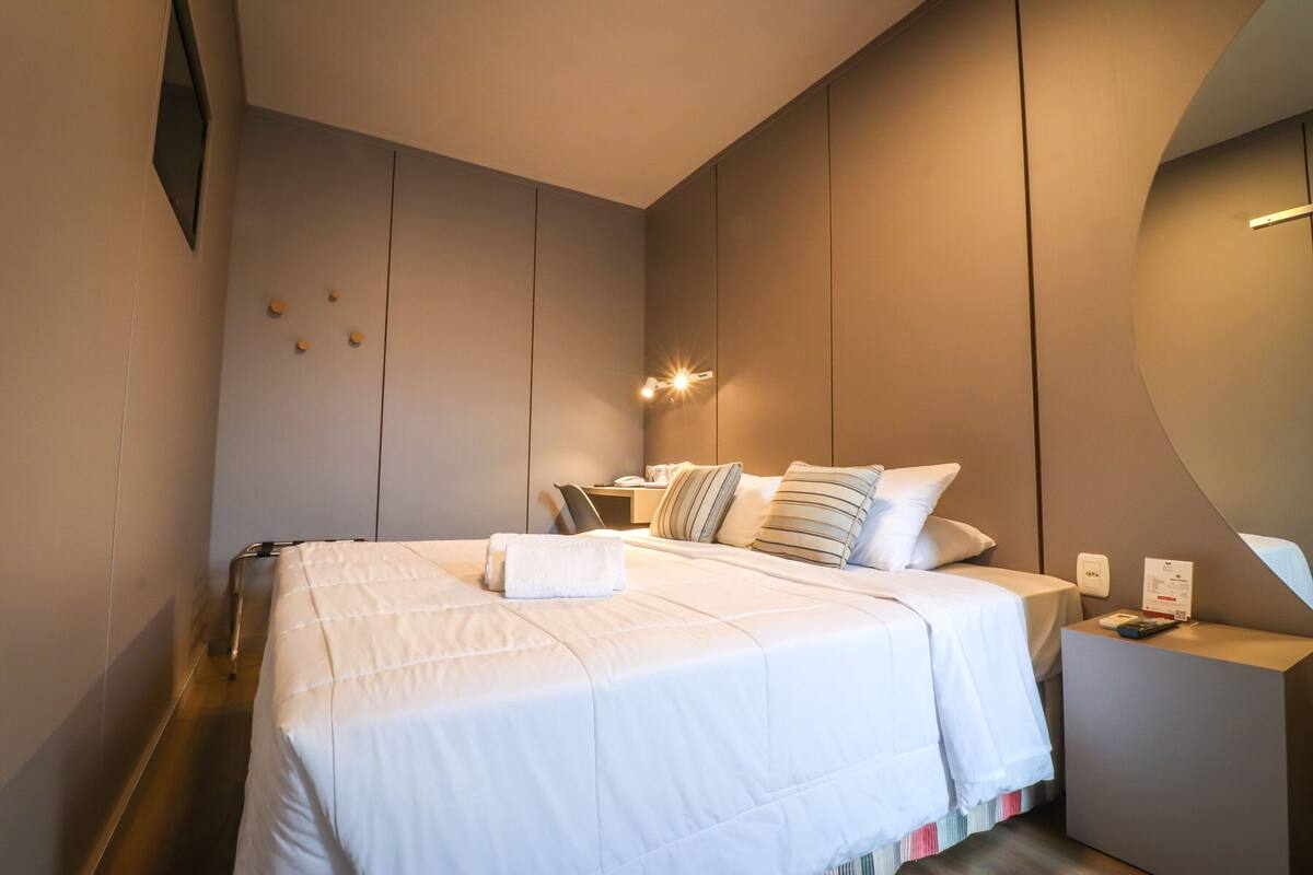 Une chambre d’hôtel moderne avec un grand lit, des tables de chevet et un luminaire fixé au mur.