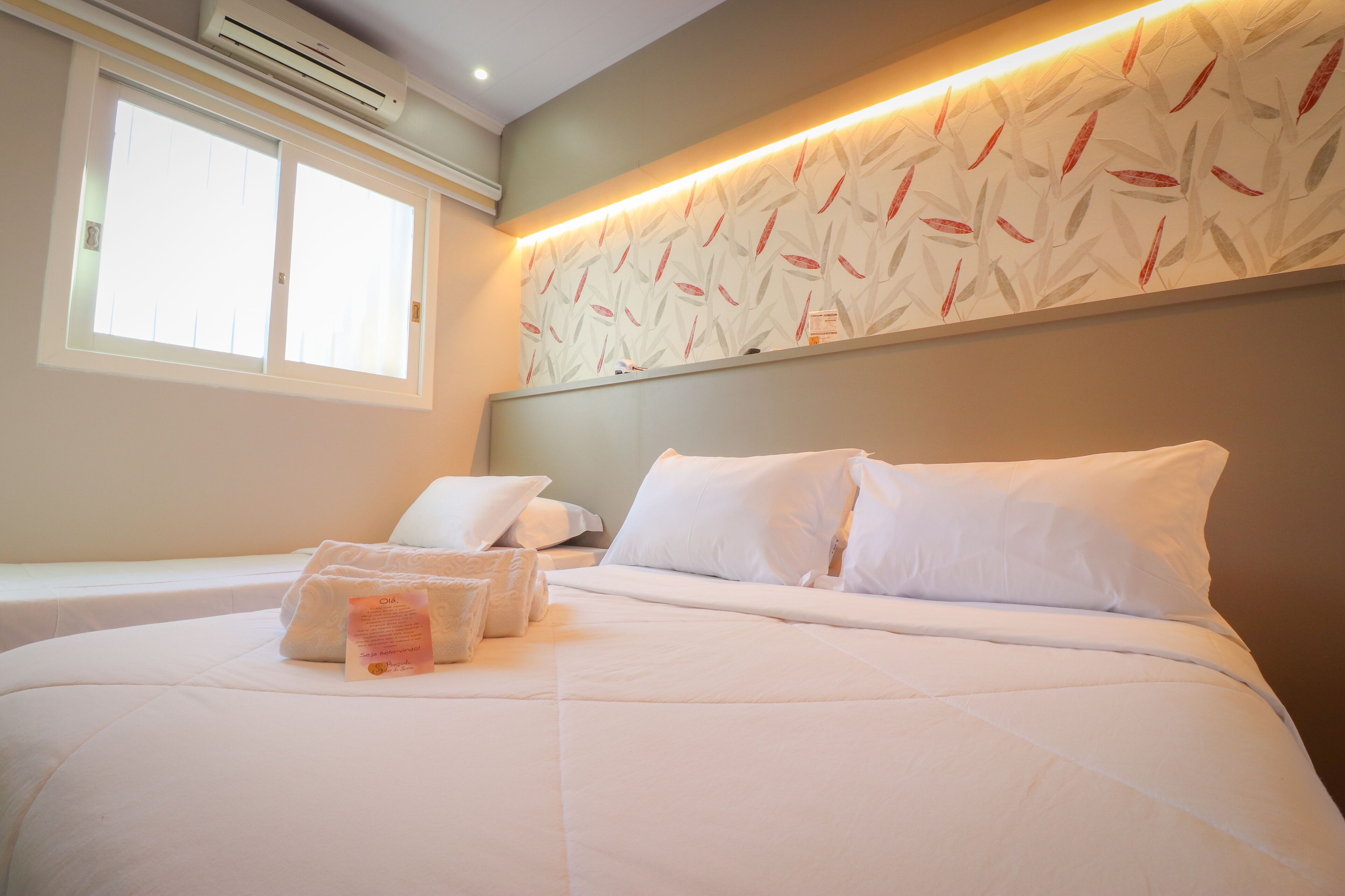 Una habitación de hotel con cama, almohadas, mesita de noche y ventana.