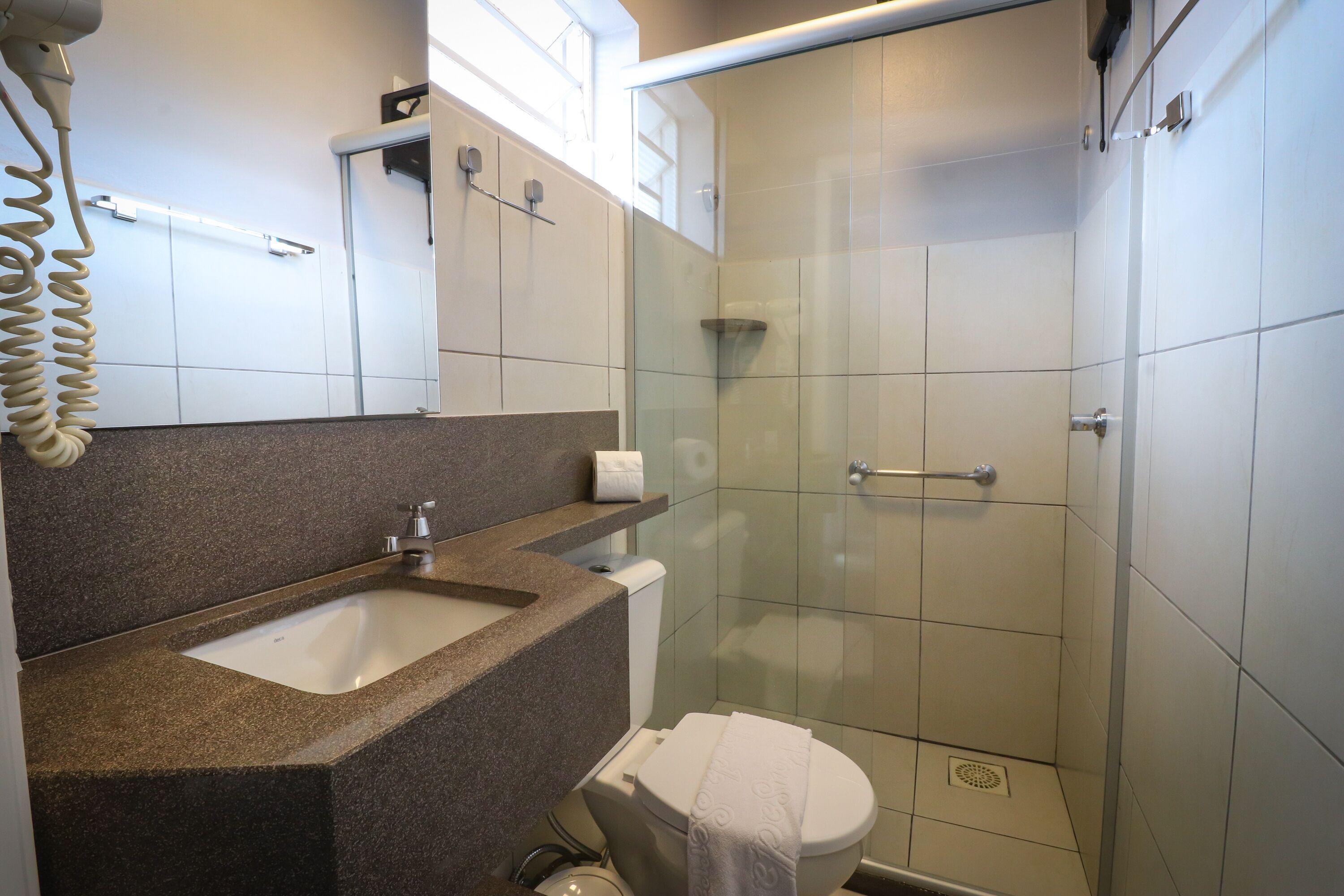 Un baño moderno con lavamanos de granito, inodoro y ducha con mampara de vidrio.