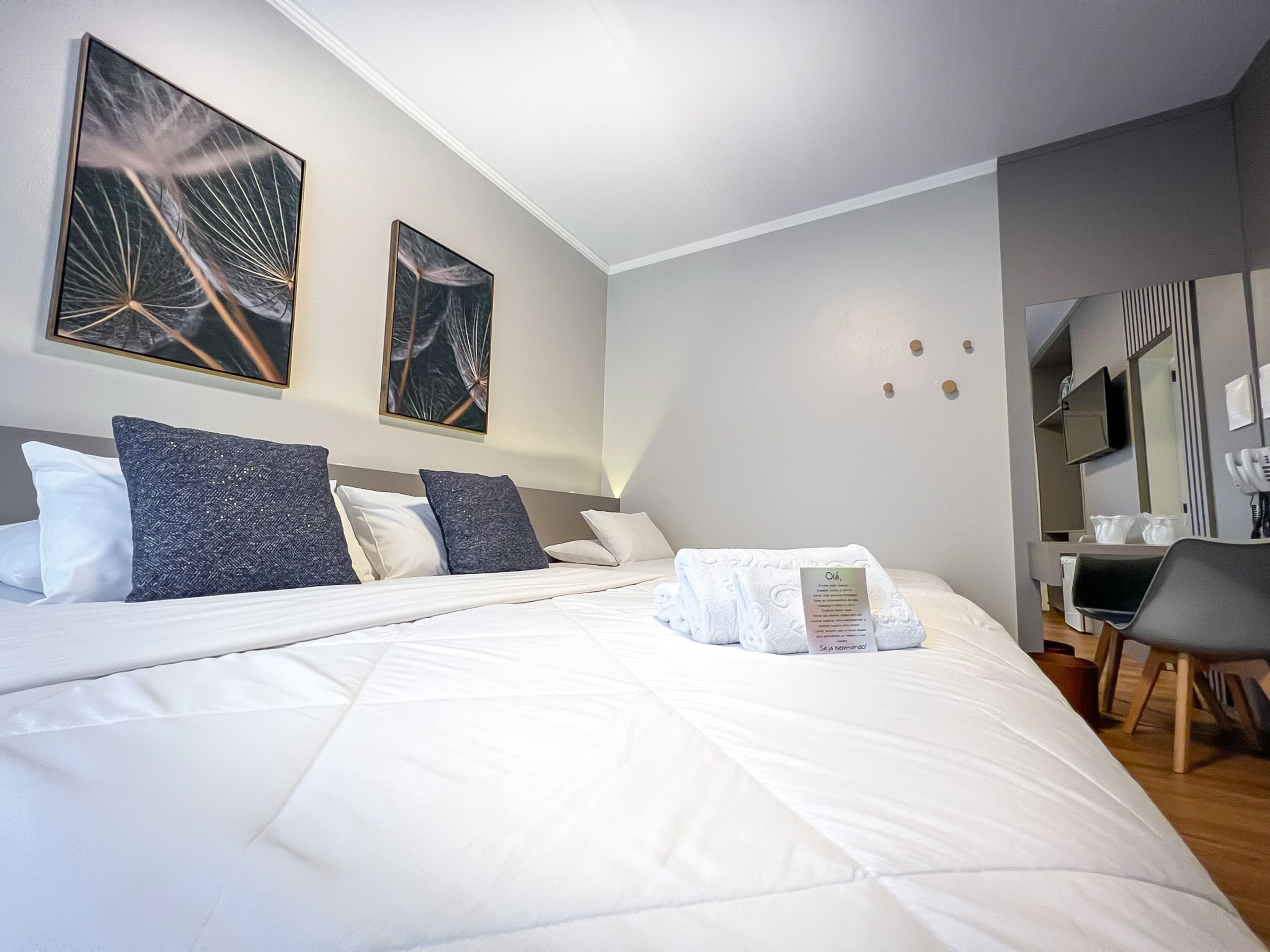 Una habitación de hotel moderna con una cama grande, dos obras de arte colgadas en la pared, un escritorio con una silla y un espejo.