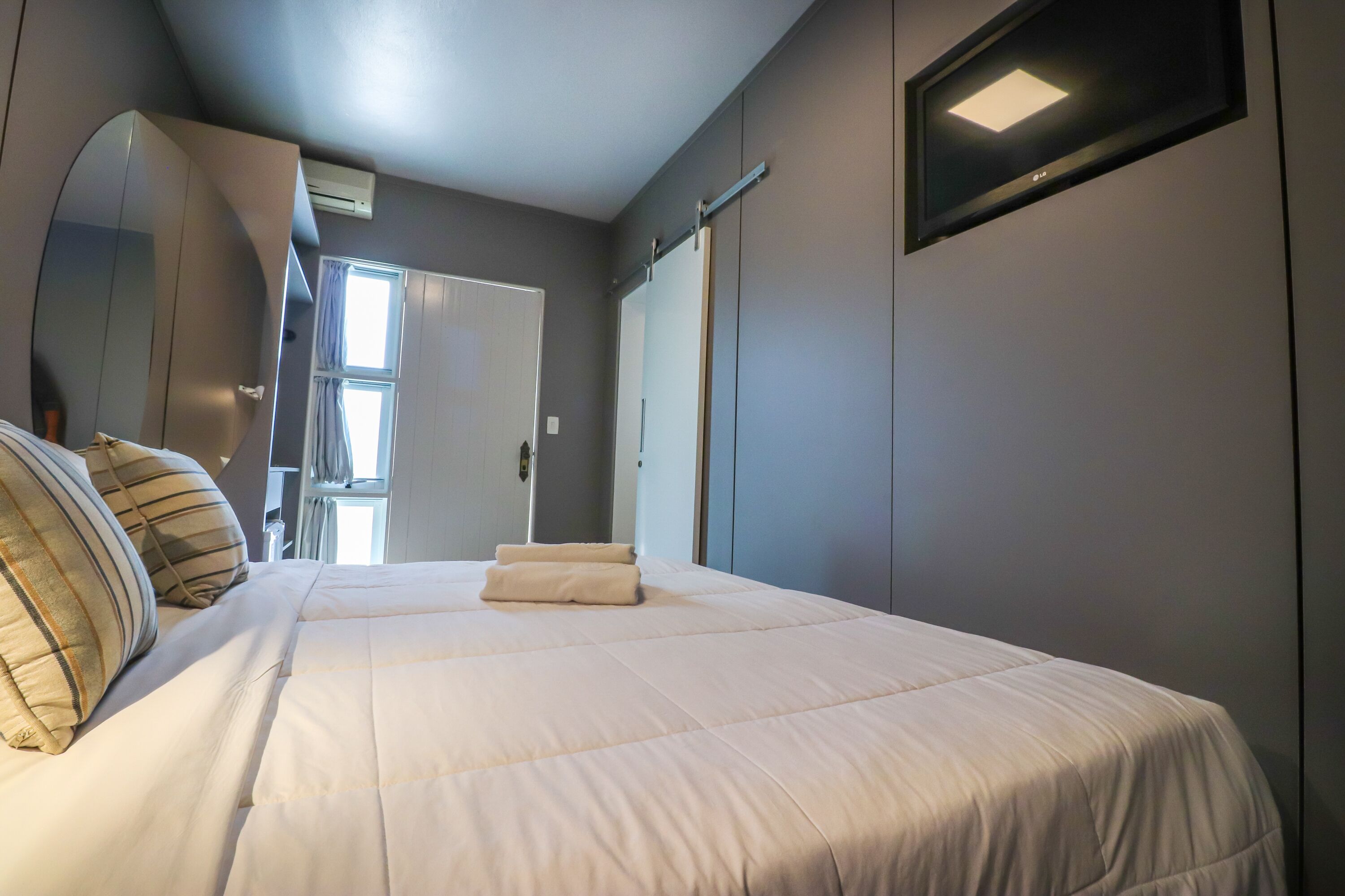 Una camera da letto con un letto, cuscini, uno specchio, un armadio e una finestra.
