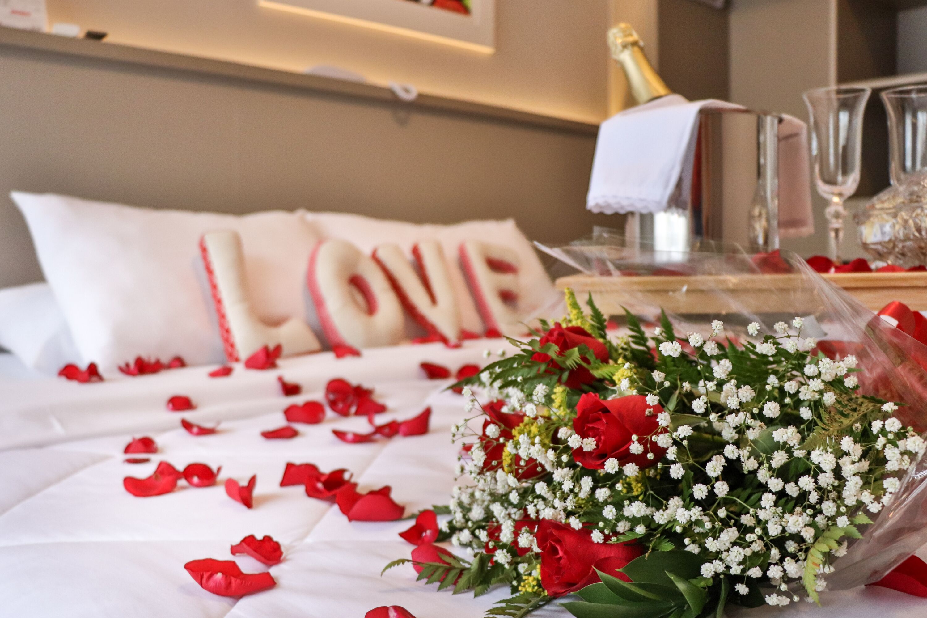 A bed with white linens, a bouquet of flowers, and a bottle of champagne.