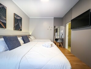 Una habitació d'hotel moderna amb dos llits, un escriptori amb una cadira, un televisor de pantalla plana i obra d'art a les parets.
