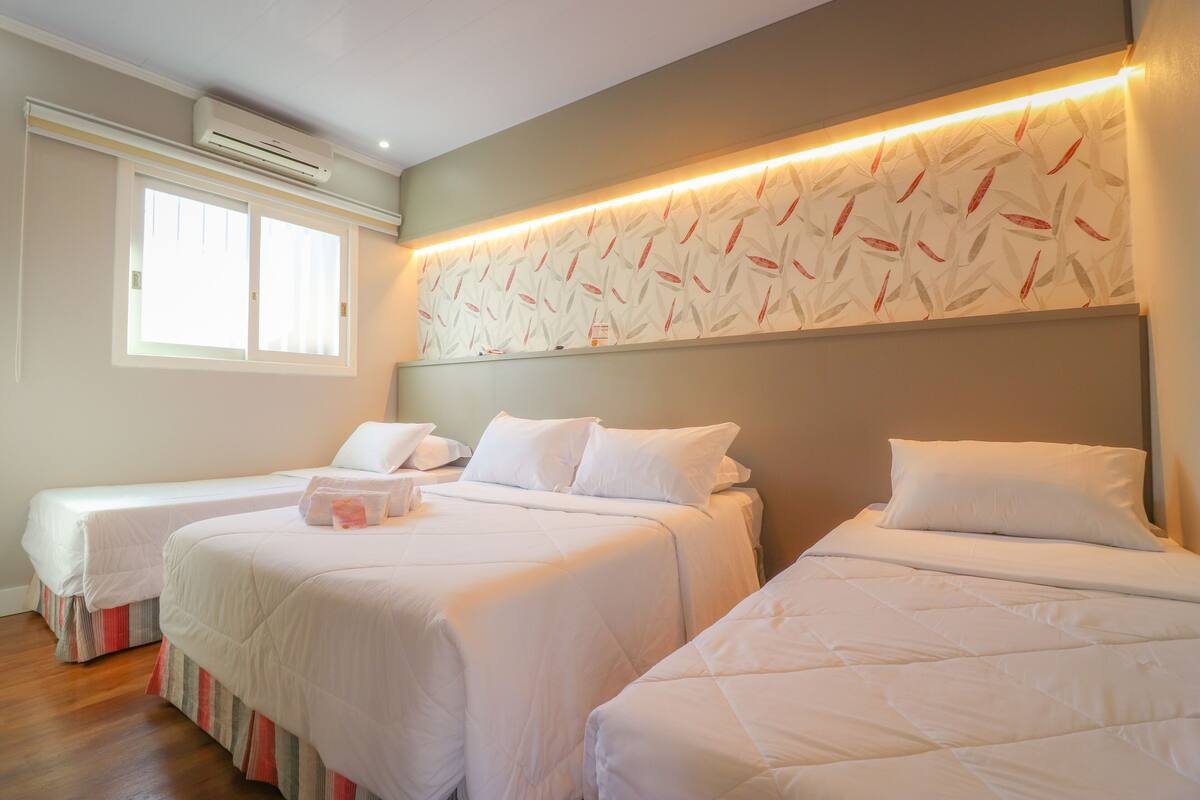 Une chambre d’hôtel avec trois lits, une fenêtre, un appareil de climatisation et un mur décoré d’un motif.