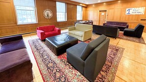 A spacious lobby with multiple seating areas, including sofas and armchairs, arranged around a central coffee table. Large windows provide natural light, and a sign indicates the location as 'Alex Hall'. - University of King's College (Halifax)