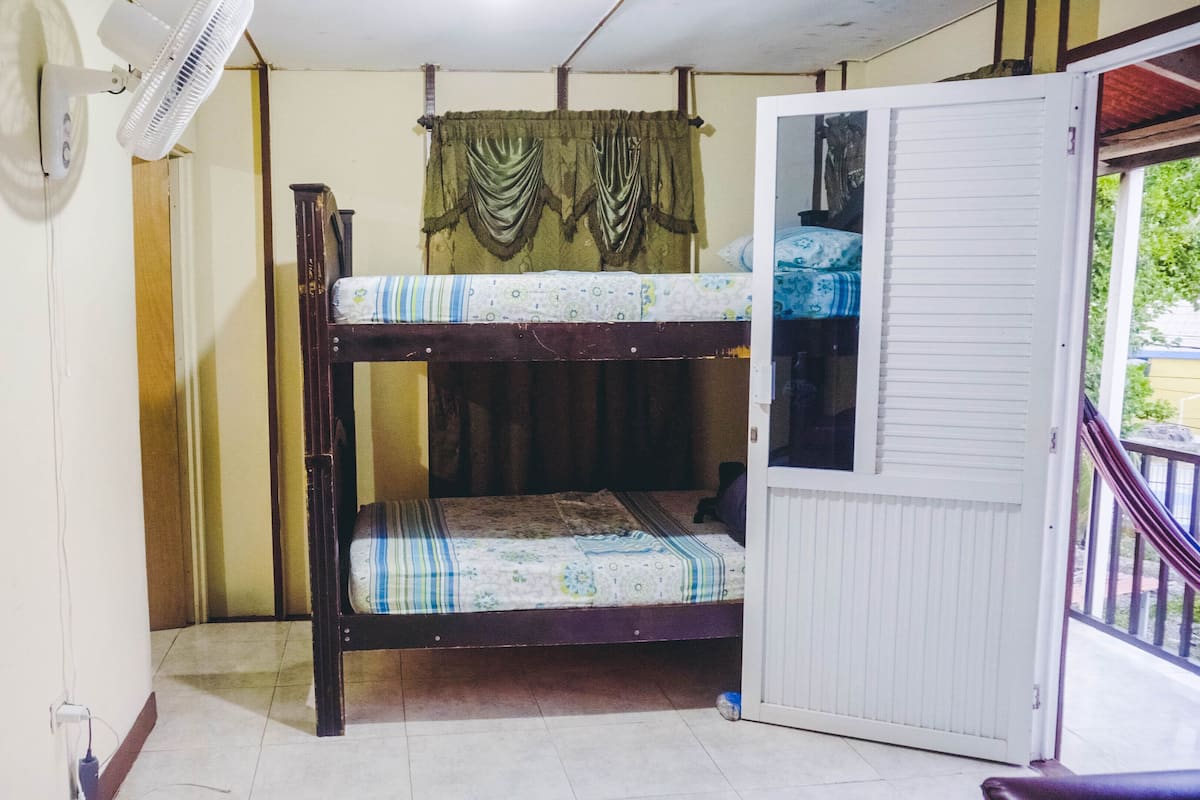 Habitación pequeña y funcional con una cama litera, una puerta blanca y una ventana con cortinas.