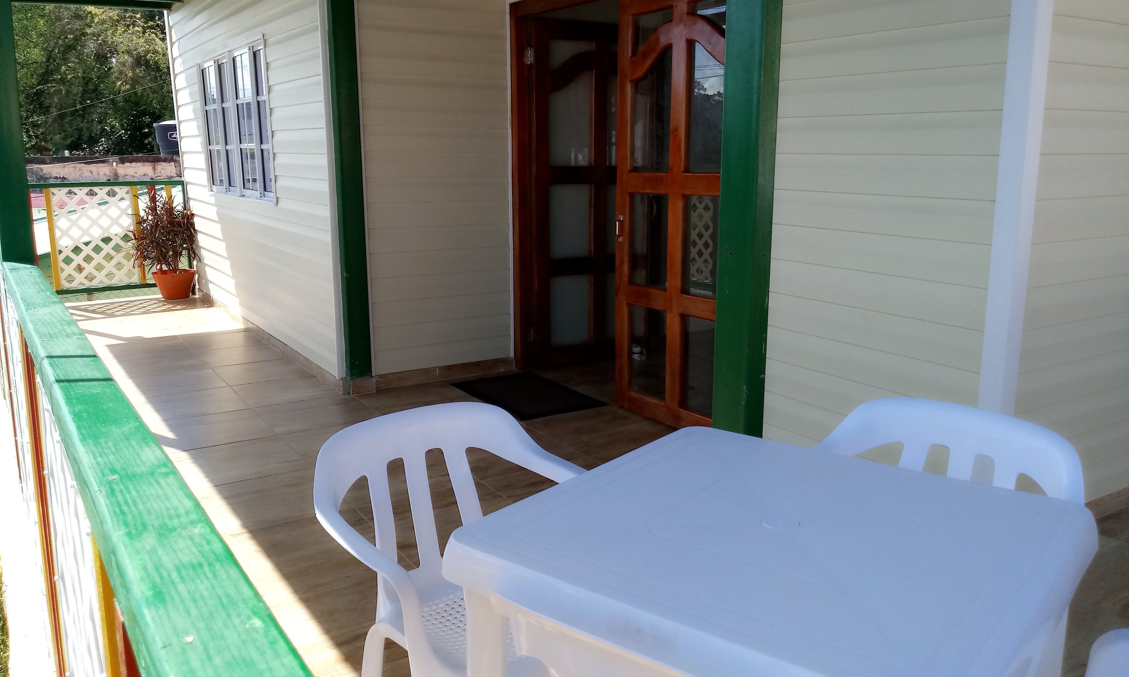 A covered outdoor seating area with a table and chairs, a wooden door, and a potted plant.