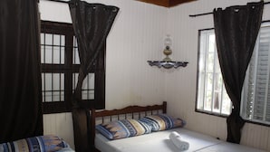 A room with two beds, each with patterned bedding and a white pillow. There is a small table with a lamp between the beds.
