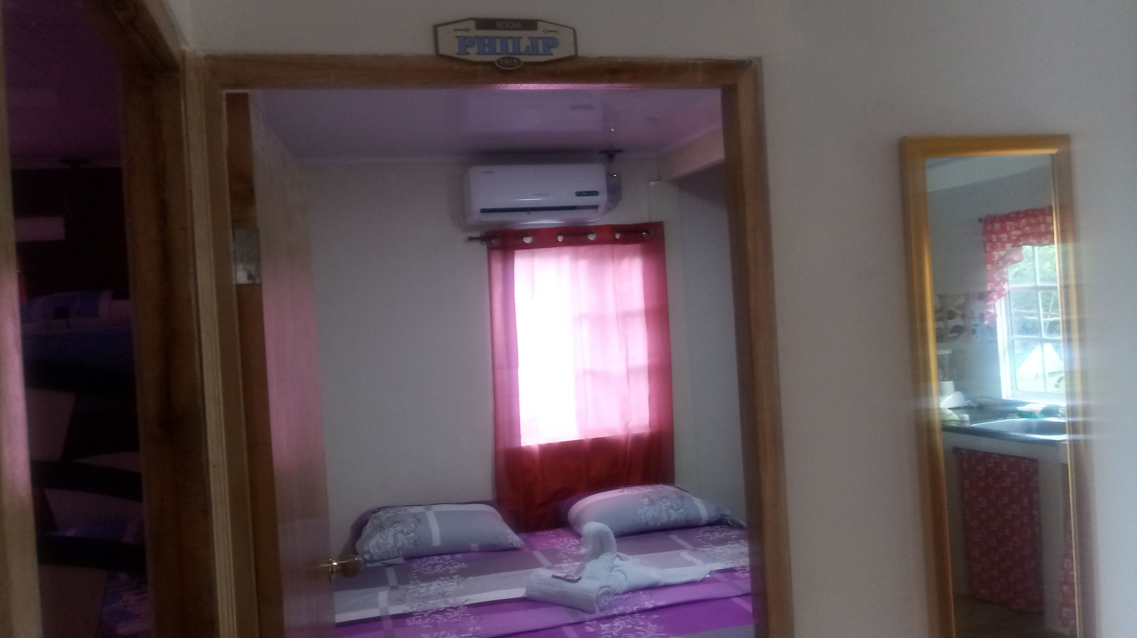 A small room with a bed, a window with a red curtain, and a ceiling-mounted air conditioner.