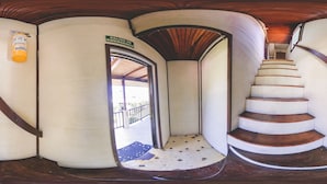 A spiral staircase with a wooden handrail and a white wall with a sign reading "SALIDA DE EMERGENCIA" (Emergency Exit).
