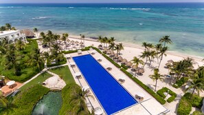 A resort with a large swimming pool, a beach, and palm trees.