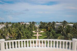 A view from a balcony with a clear sky, palm trees, and a distant body of water.