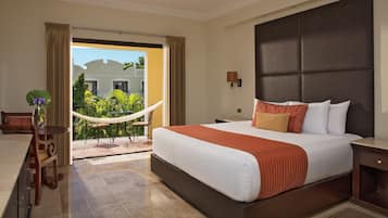 A hotel room with a large bed, a ceiling fan, a view of a building and greenery outside, and a balcony with a hammock.