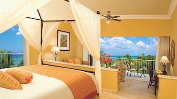 A bedroom with a four-poster bed, a balcony with a view of the ocean, and a ceiling fan.