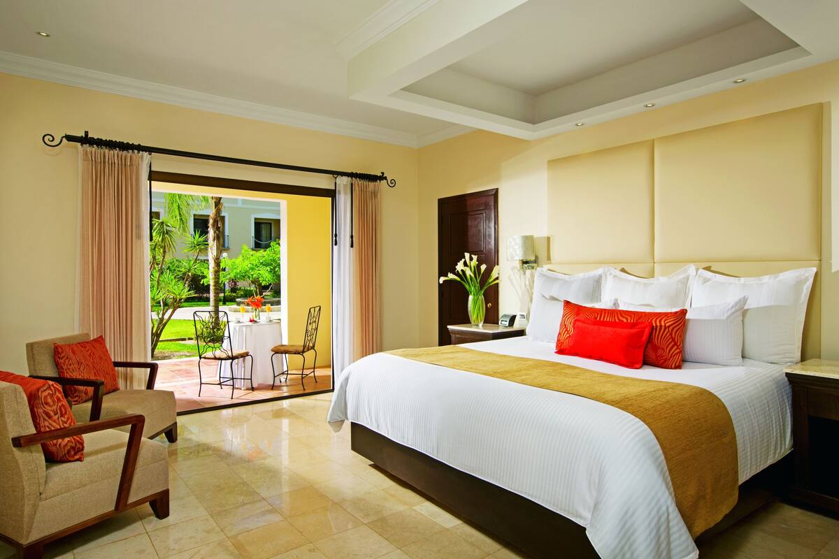 A hotel room with a large bed, a chair, a table, and a view of the outdoors.