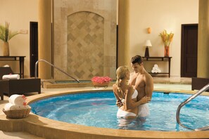 A couple by a pool with a tiled wall, a potted plant, and a basket of towels.