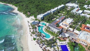 An aerial view of a resort with a large swimming pool, beachfront, and lush greenery. - Dreams Tulum Resort & Spa - All Inclusive (Tulum)