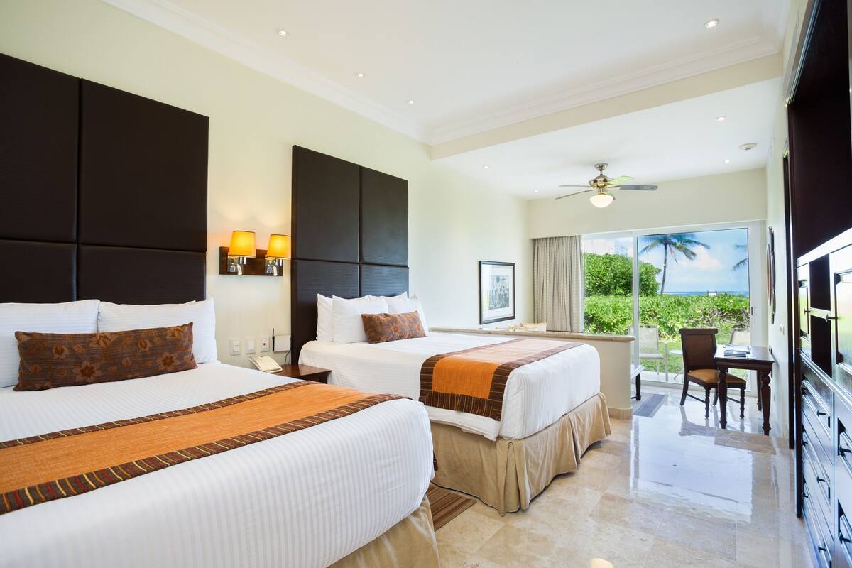 A hotel room with two beds, a balcony with a view, and a desk with a chair.