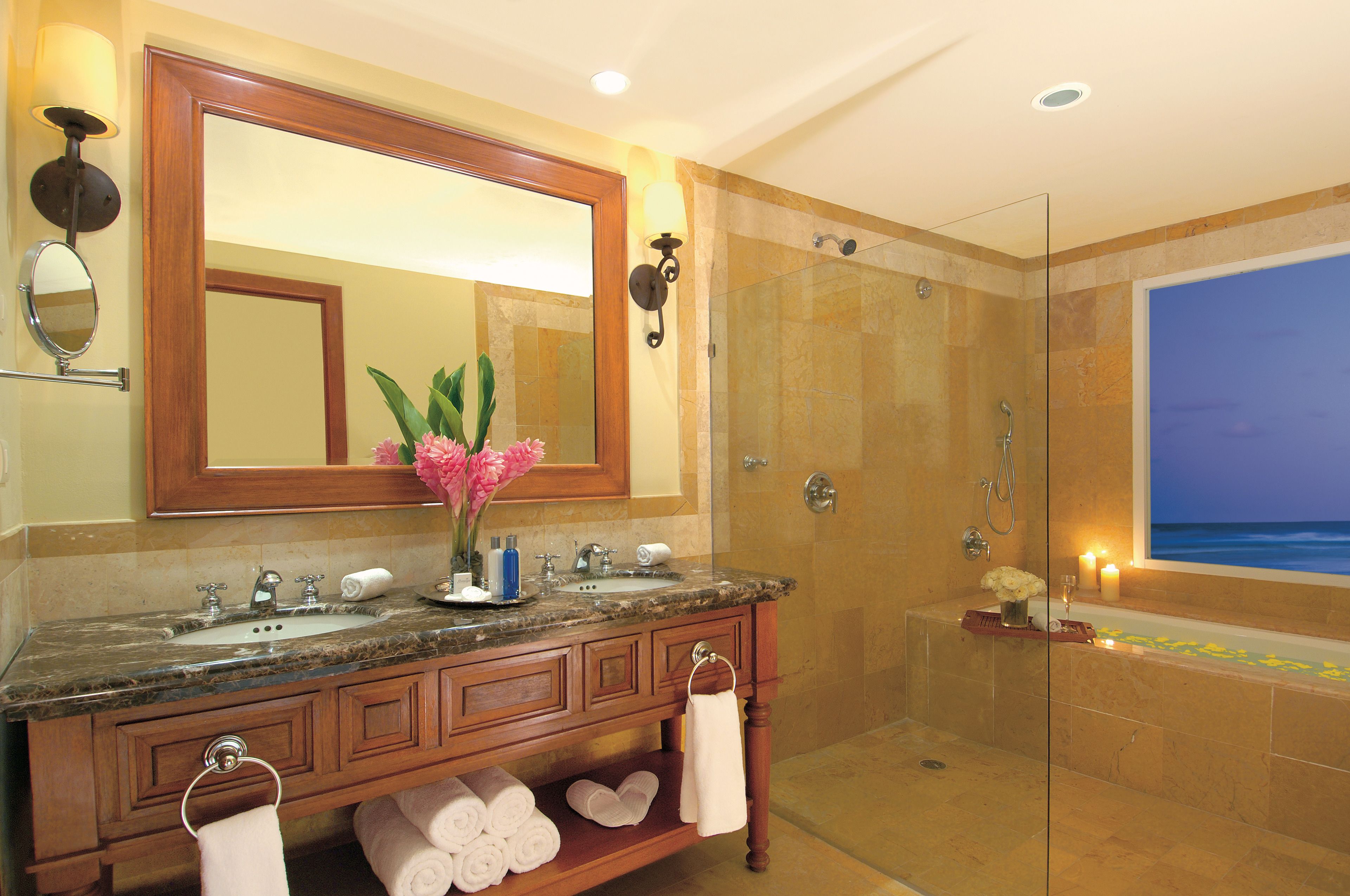 A bathroom with a marble sink, a large mirror, a glass-enclosed shower, and a bathtub with candles.