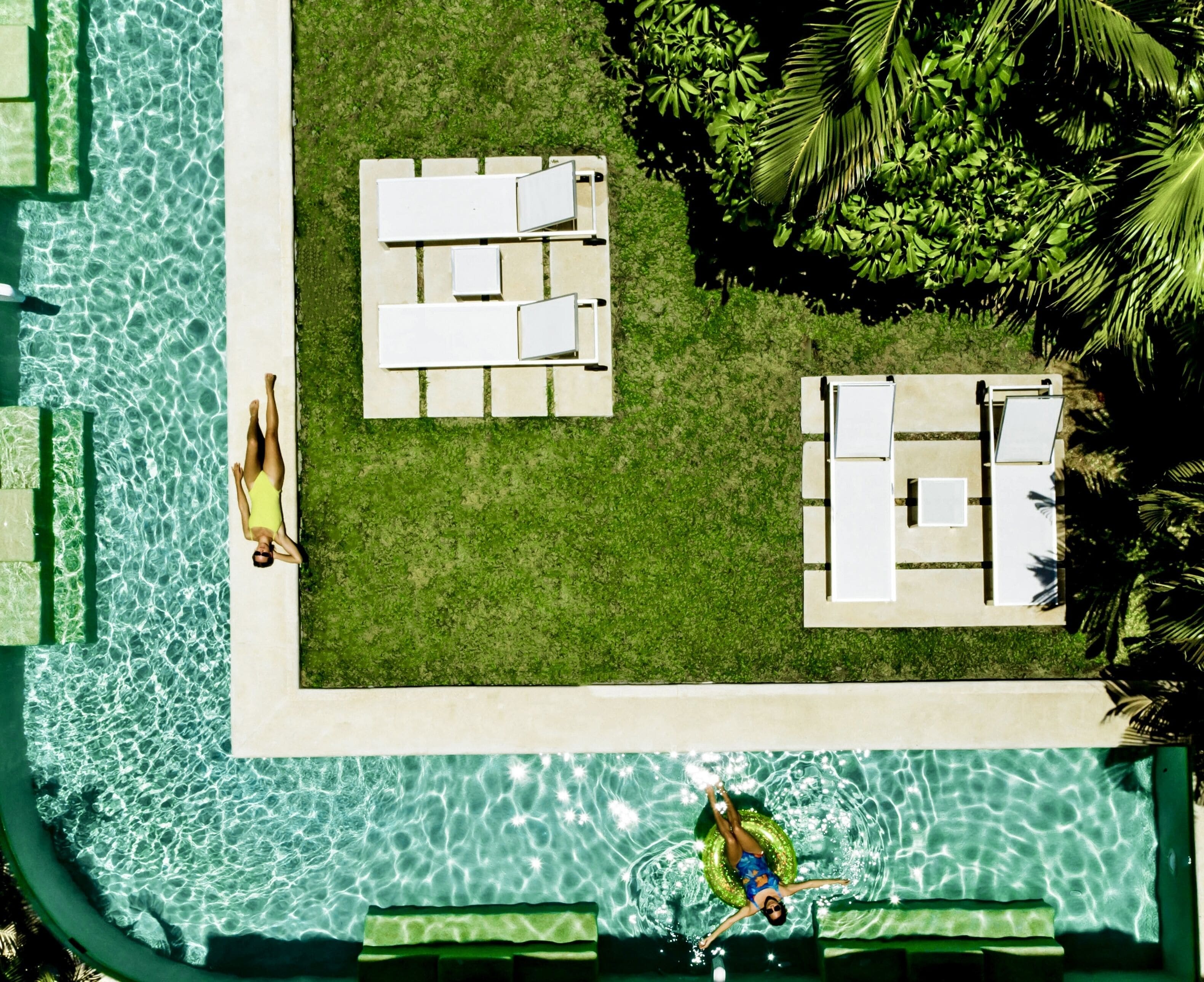 An aerial view of a swimming pool with two lounge areas, one with a grassy deck and the other with a paved deck.