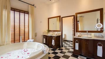A bathroom with a checkered floor, a bathtub with rose petals, and two sinks with mirrors.