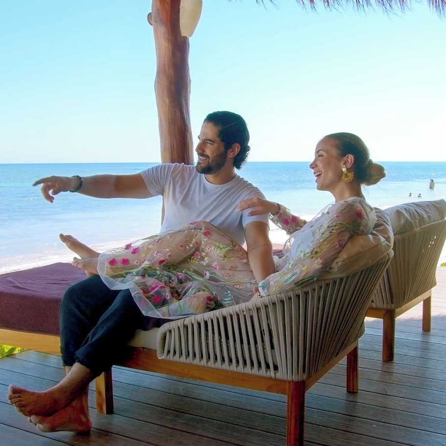 A couple sitting on a wooden deck overlooking a beach.