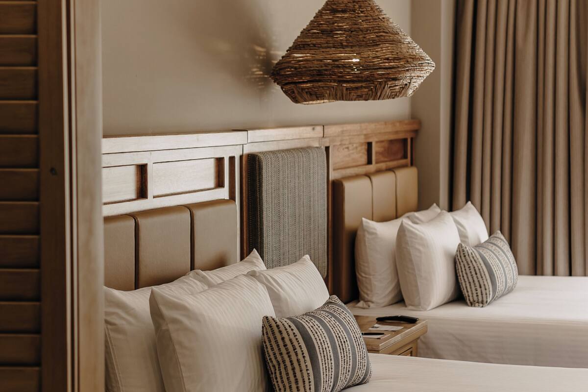 A hotel room with a large mirror reflecting a bed, a hanging woven light fixture, and a view of the outside curtains.